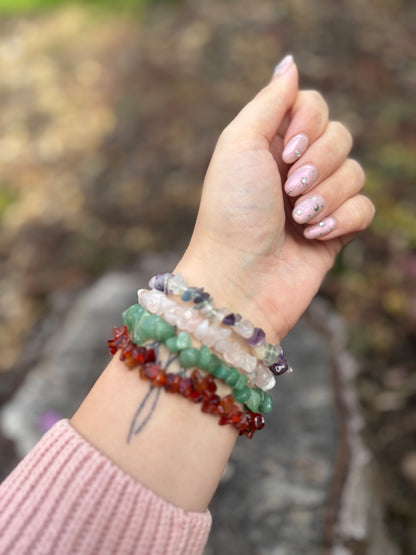 Hand wearing multiple beaded bracelets with a blurred natural background