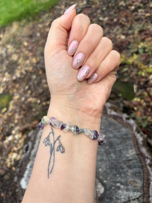 Hand wearing a beaded bracelet with a tattoo on the wrist, against a natural background. Fluorite crystal bracelet for mental clarity, focus, and calm. Wearable ritual for meditation, study, and balanced energy.